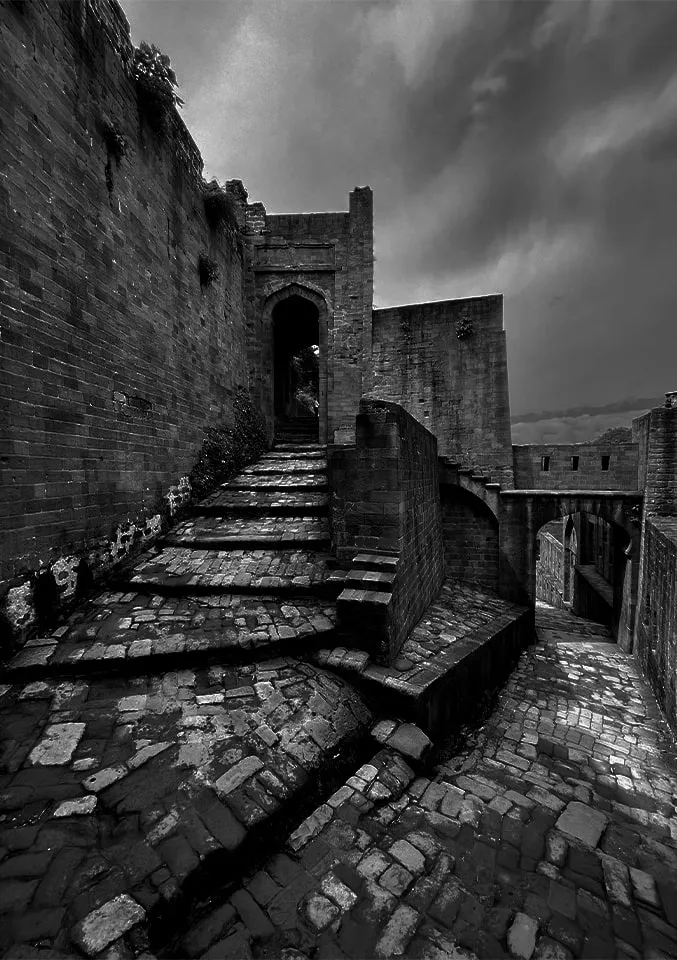 Black-and-white photograph of worn stone steps and gateways at Kangra Fort under a stormy sky.